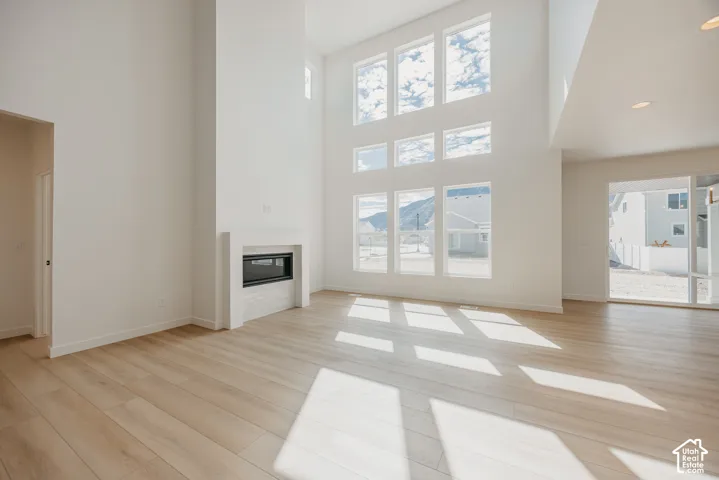 Vaulted ceiling with extensive window array, linear fireplace with tiled surround, wood-finish flooring, and recessed lighting