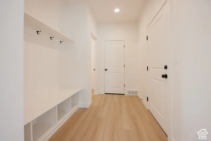Built-in storage bench with cubbies, upper shelf with hooks, light wood-finish flooring, and white paneled doors with matte black hardware