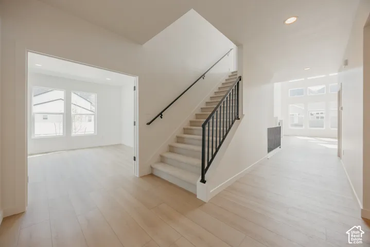 Open-concept entryway with light wood-finish flooring, a carpeted staircase with a black metal railing, and high ceilings