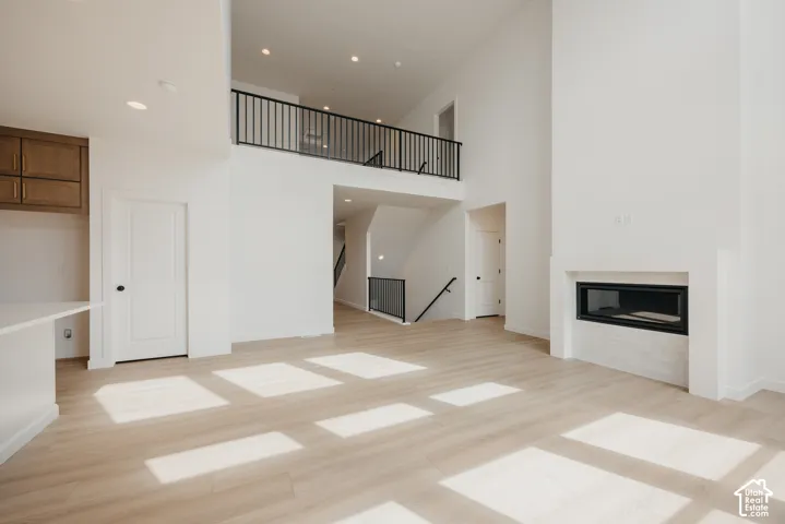 Two-story living area with light wood-finish flooring, a built-in linear fireplace with a textured surround, and a second-story interior balcony with black metal railing