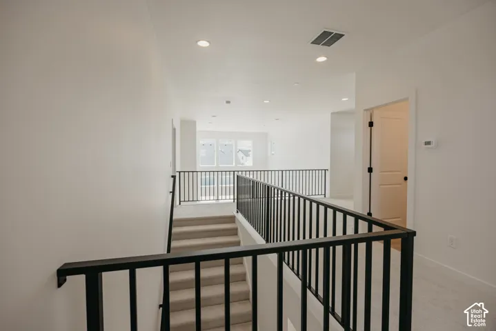 Carpeted staircase with black metal railings, leading to a carpeted landing featuring recessed lighting and a single door