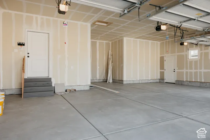 Spacious garage featuring polished concrete flooring, recessed lighting throughout, drywall construction with vertical stud detailing, and multiple entry points including a standard garage door and pedestrian access door