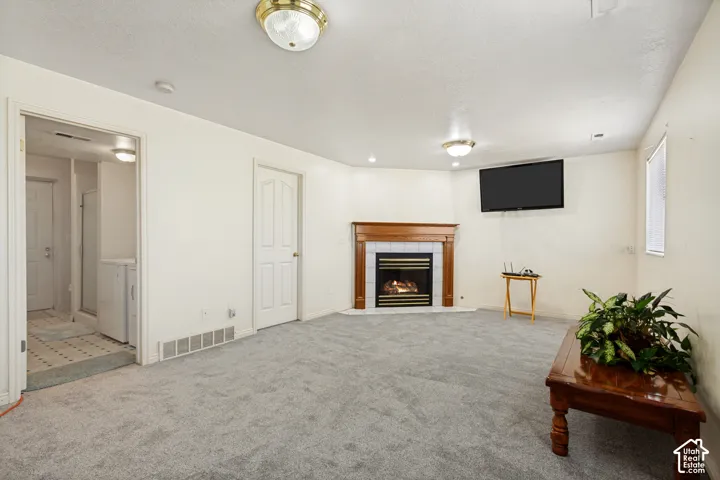 Recessed lighting, fireplace with wood mantel, tiled fireplace surround, light-colored carpeting, and a built-in wall television mount