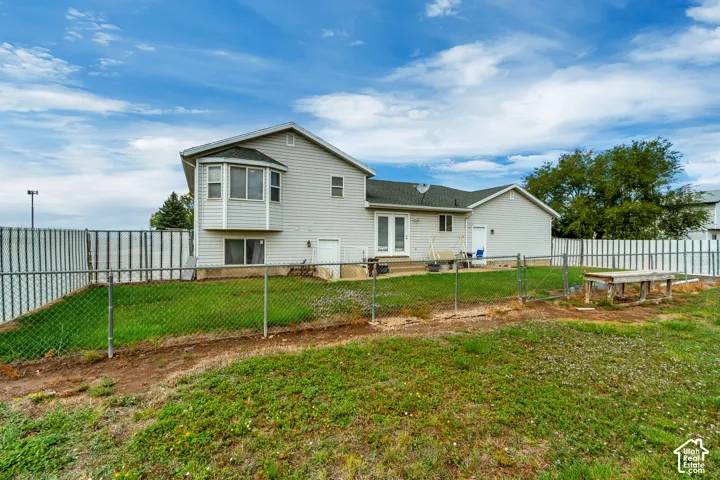 Rear exterior featuring a bay window, double French doors, chain-link fencing, and a separate side entrance