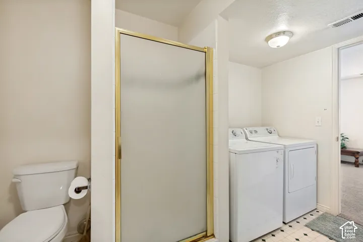 Bathroom featuring a white toilet, enclosed shower with a gold-finish frame, and an adjacent laundry area with a washer and dryer