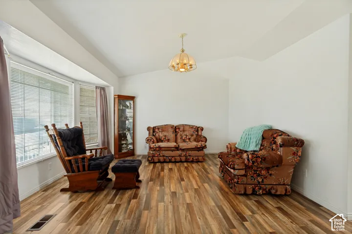 Vaulted ceiling, wood-finish flooring, white walls, large bay window, and a built-in light fixture