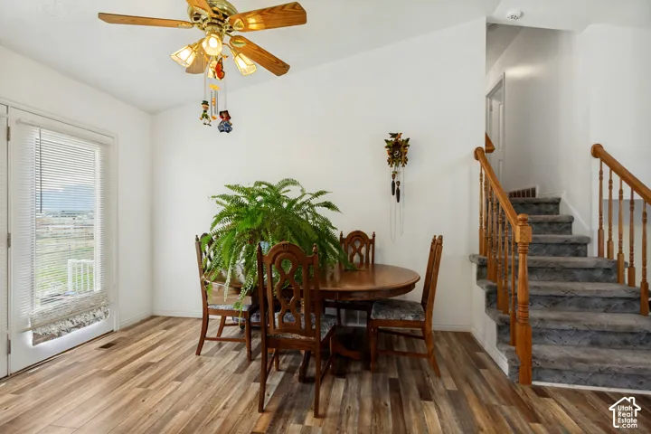 Vaulted ceiling featuring a ceiling fan with light fixture, wood-finish flooring, and a door with horizontal blinds