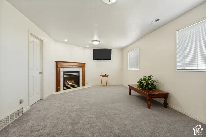 Corner fireplace with a wood mantel and tile surround, recessed lighting, and soft grey carpeting