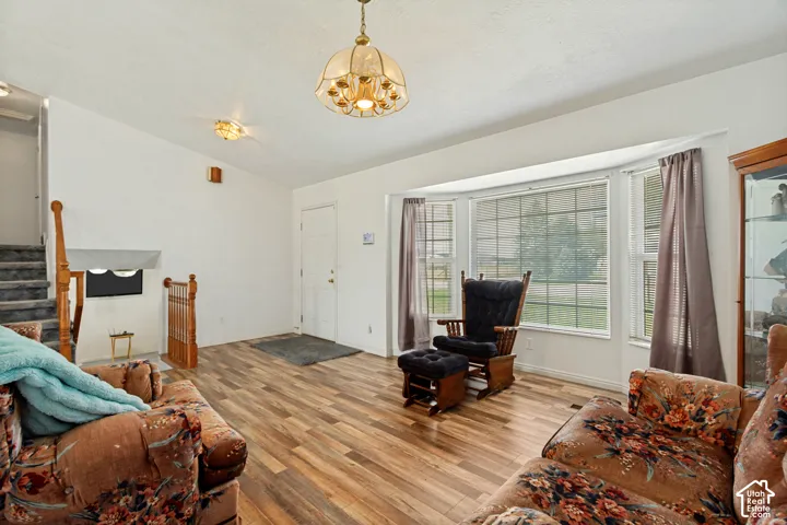 Living space featuring wood-finish flooring, a bay window with natural light, a ceiling-mounted light fixture, and a staircase with wood railings