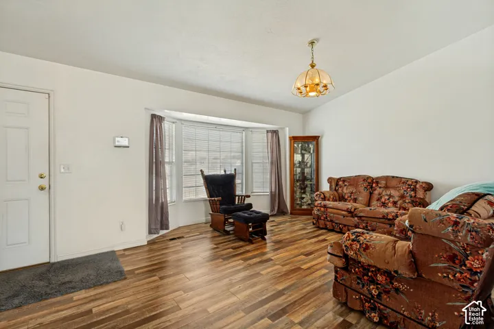 Vaulted ceiling, wood-finish flooring, bay window, white paneled entry door, and a decorative ceiling fixture