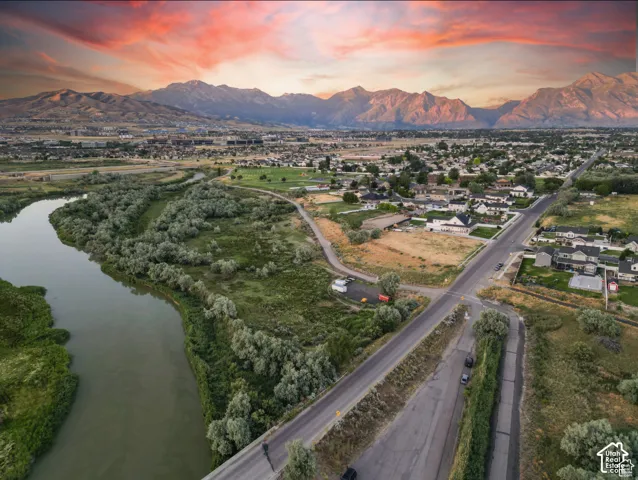 Expansive natural landscape featuring a prominent river, lush green foliage, distinct residential areas, and distant mountainous terrain