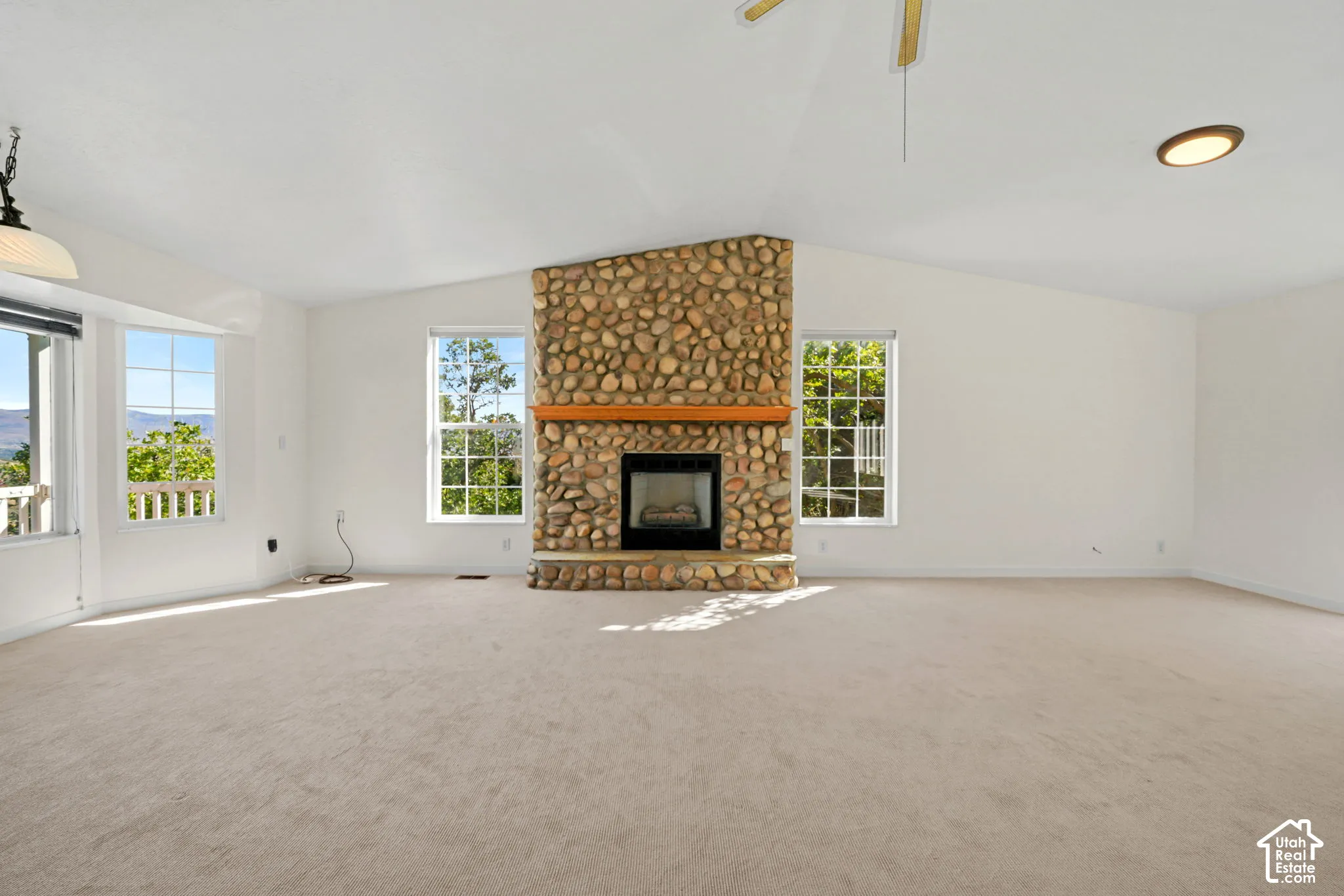 Vaulted ceiling, large windows, stone fireplace with wood mantel, and carpeting