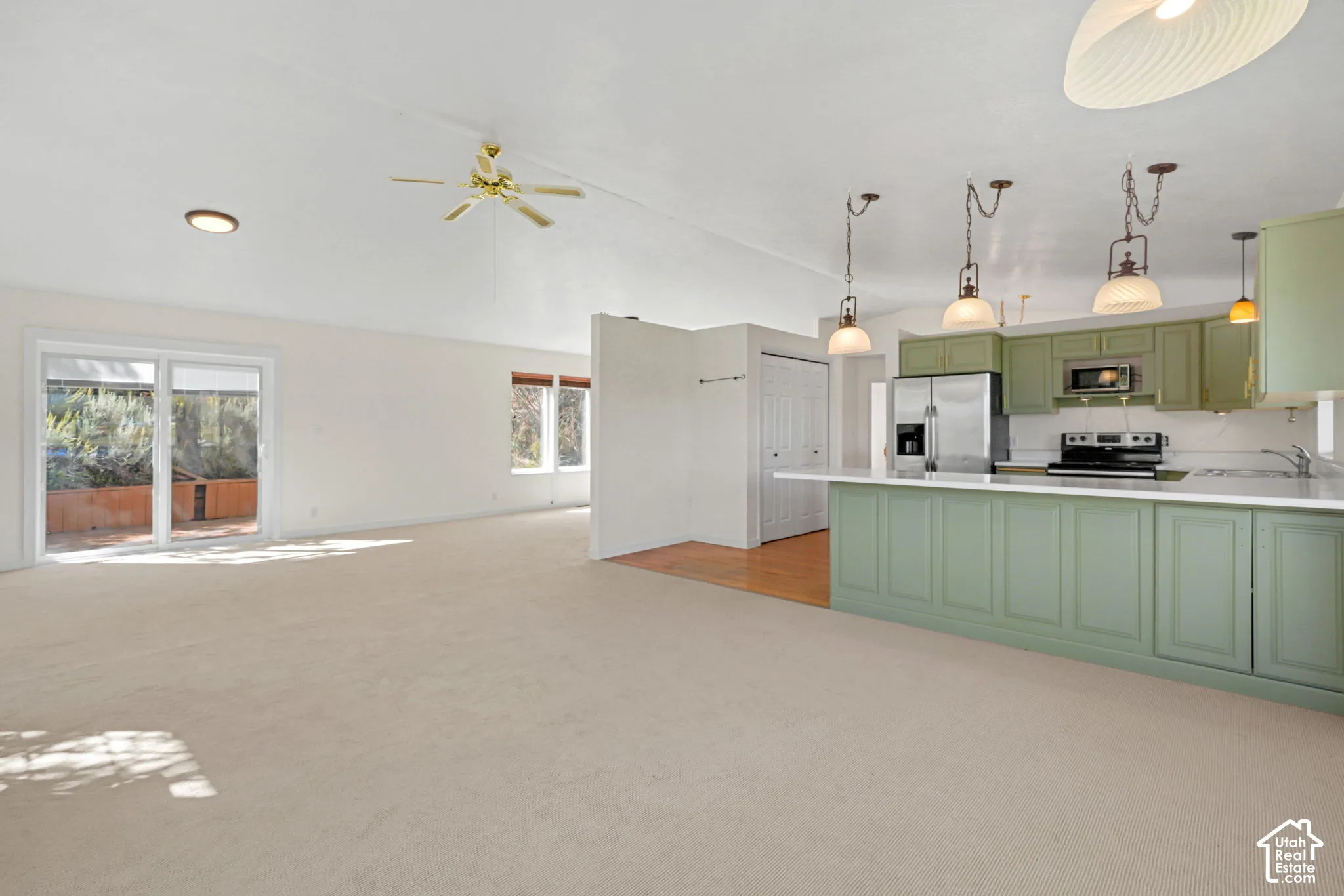 Open-concept living space with sliding glass doors, ceiling fan, and carpet flooring