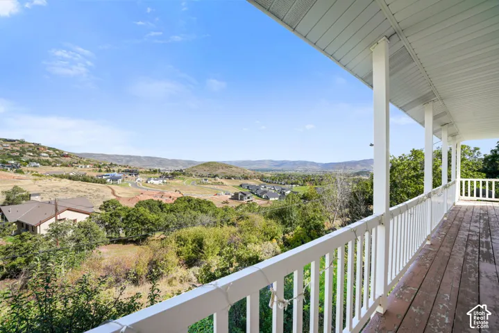 Expansive covered deck with wood flooring and white railing, featuring distant mountain scenery and surrounding properties