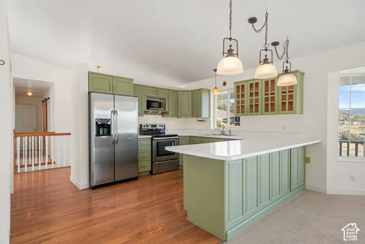 Kitchen with wood-finish flooring, green cabinetry, white countertops, and stainless steel appliances