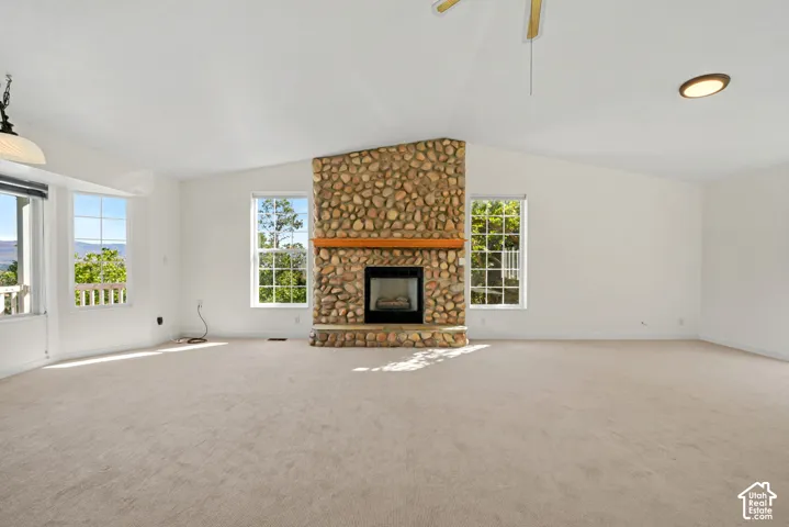 Vaulted ceiling, large windows, stone fireplace with wood mantel, and carpeting