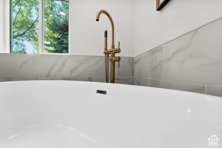 Spa-inspired primary bathroom featuring a freestanding soaking tub with integrated deck-mounted filler, brushed brass fixtures, and large-format marble-look tile surround