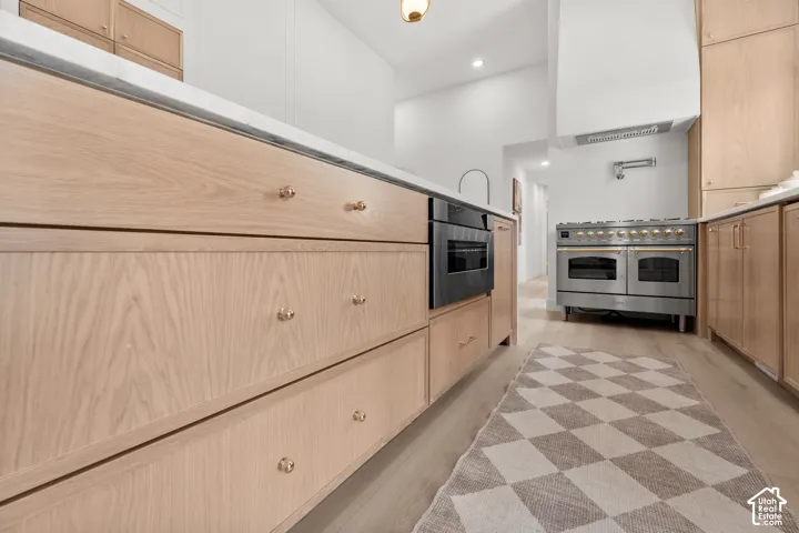 Hardwood flooring, light wood cabinetry, white countertops, built-in oven, and stainless steel range