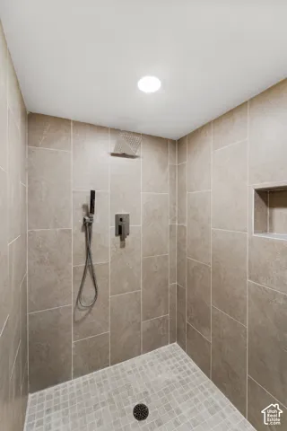 Walk-in shower featuring large format wall tiles, a built-in shower niche, and a rain shower head with a handheld sprayer