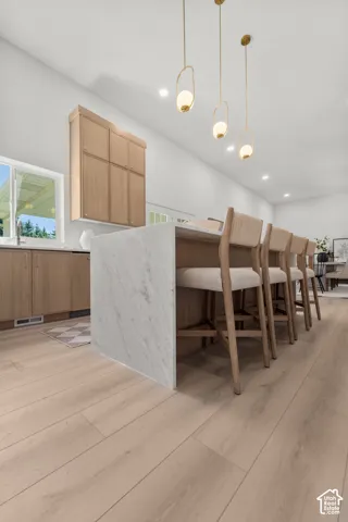 Kitchen island with waterfall edge, wood-finish flooring, recessed lighting, and decorative pendant lights