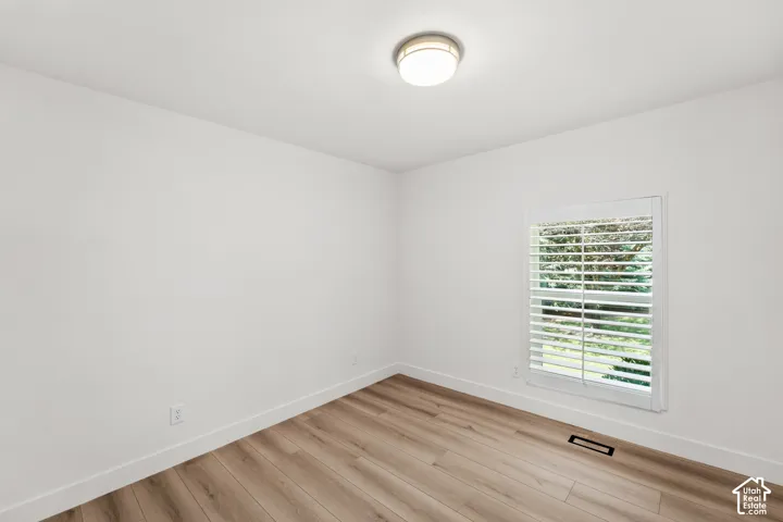White walls, wood-finish flooring, and a single window with white plantation shutters