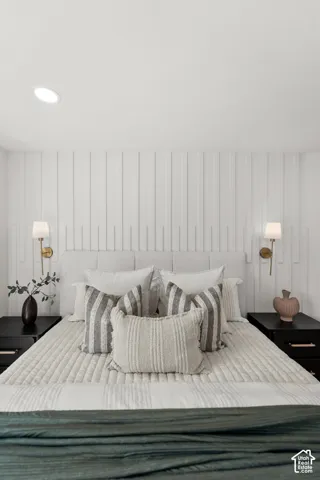 Master bedroom featuring a vertical shiplap accent wall, layered bedding with striped and patterned pillows, flanking wall-mounted sconces with brass fixtures, black nightstands, and a geometric patterned area rug anchoring the space