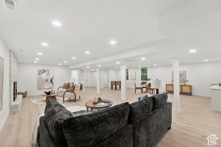 Expansive lower-level space featuring recessed lighting, light wood-finish flooring, a white brick fireplace, and structural support columns