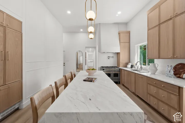 Expansive kitchen island with a stone countertop, featuring a built-in range, a single basin sink, wood-finish cabinetry, and decorative wall paneling