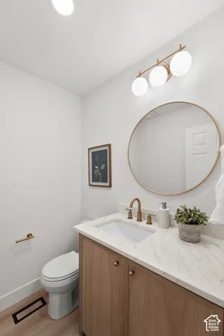Modern vanity with a light wood-finish cabinet, white countertop, and gold-finish fixtures