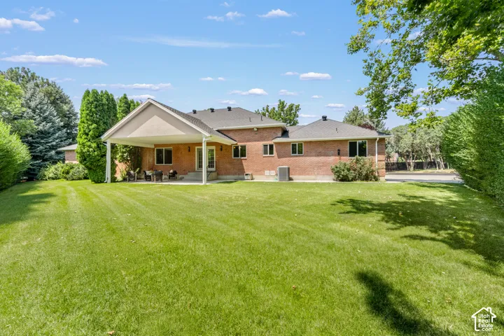 Expansive lawn with a covered patio, brick exterior, and mature perimeter trees