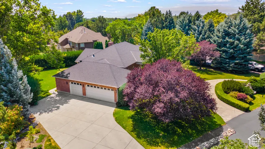Brick exterior with a three-car garage, concrete driveway, and mature landscaping