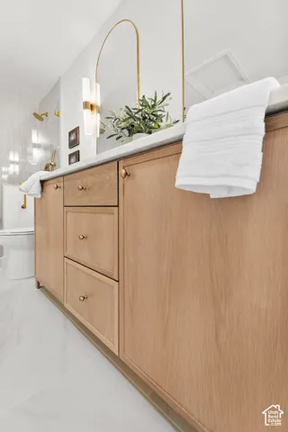 Light wood-finish vanity with brass hardware, a white countertop, and an arched brass-framed mirror