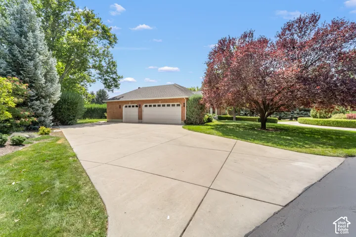 Brick exterior garage structure with two garage doors, a concrete driveway, and surrounding mature landscaping