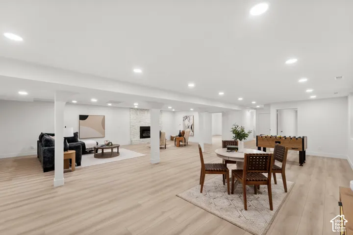 Spacious finished lower level with light wood-finish flooring, recessed lighting, and a white stone fireplace surround