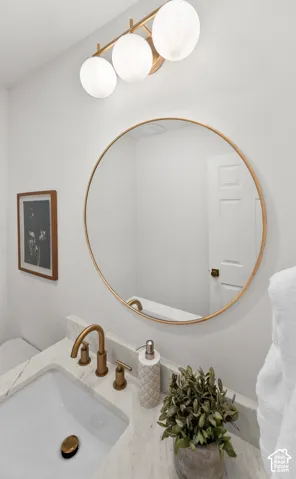White vanity with a rectangular undermount sink, gold-tone fixtures, and a white countertop
