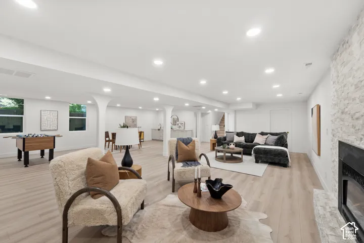 Spacious lower level featuring recessed lighting, light wood-finish flooring, a stone-clad fireplace, and a built-in wet bar with a round sink