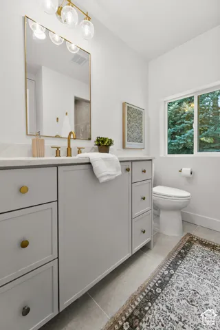 Bathroom featuring a light gray vanity with brass hardware, a gold-framed mirror, a modern brass light fixture, and a window