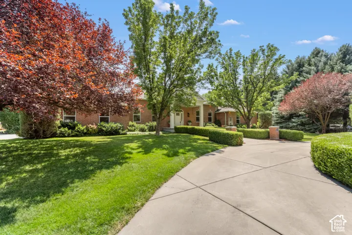 Brick exterior residence with a concrete driveway, manicured lawn, and mature trees