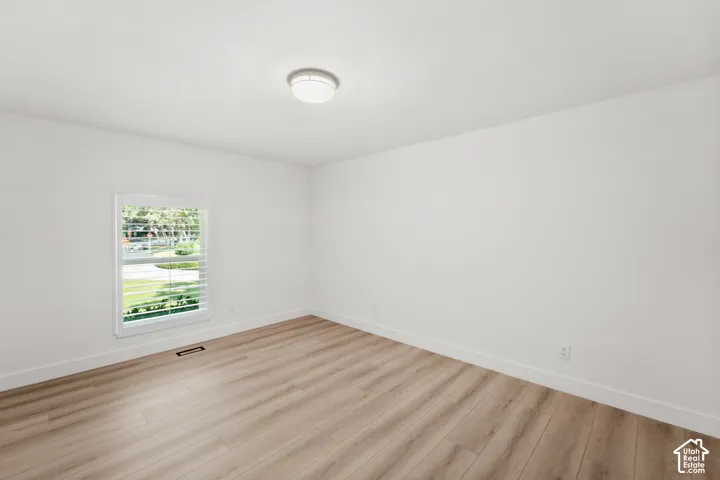 Wood-finish flooring, white walls, and a window with plantation shutters