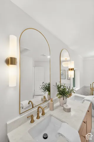 Dual arched mirrors, dual vanity with undermount sinks, stone-finish countertop, and brushed gold fixtures