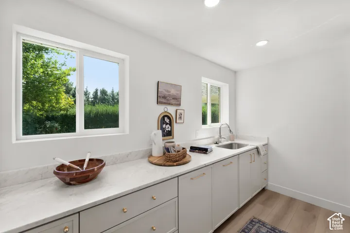 Recessed lighting illuminating a built-in sink with a gooseneck faucet, white cabinetry, and light-toned countertops
