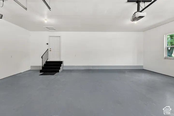 Spacious garage with light grey finished flooring, white painted walls, and an interior door with a black handrail