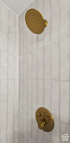 Shower featuring a gold-tone rain shower head and coordinating controls, set against vertically oriented rectangular wall tiles