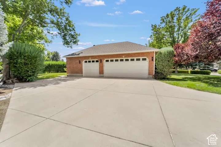 Brick exterior structure featuring two garage doors, a concrete driveway, and surrounding greenery