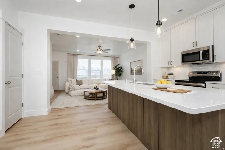 Kitchen with a wood-finish island, white countertop, pendant lighting, stainless steel appliances, and a tile backsplash