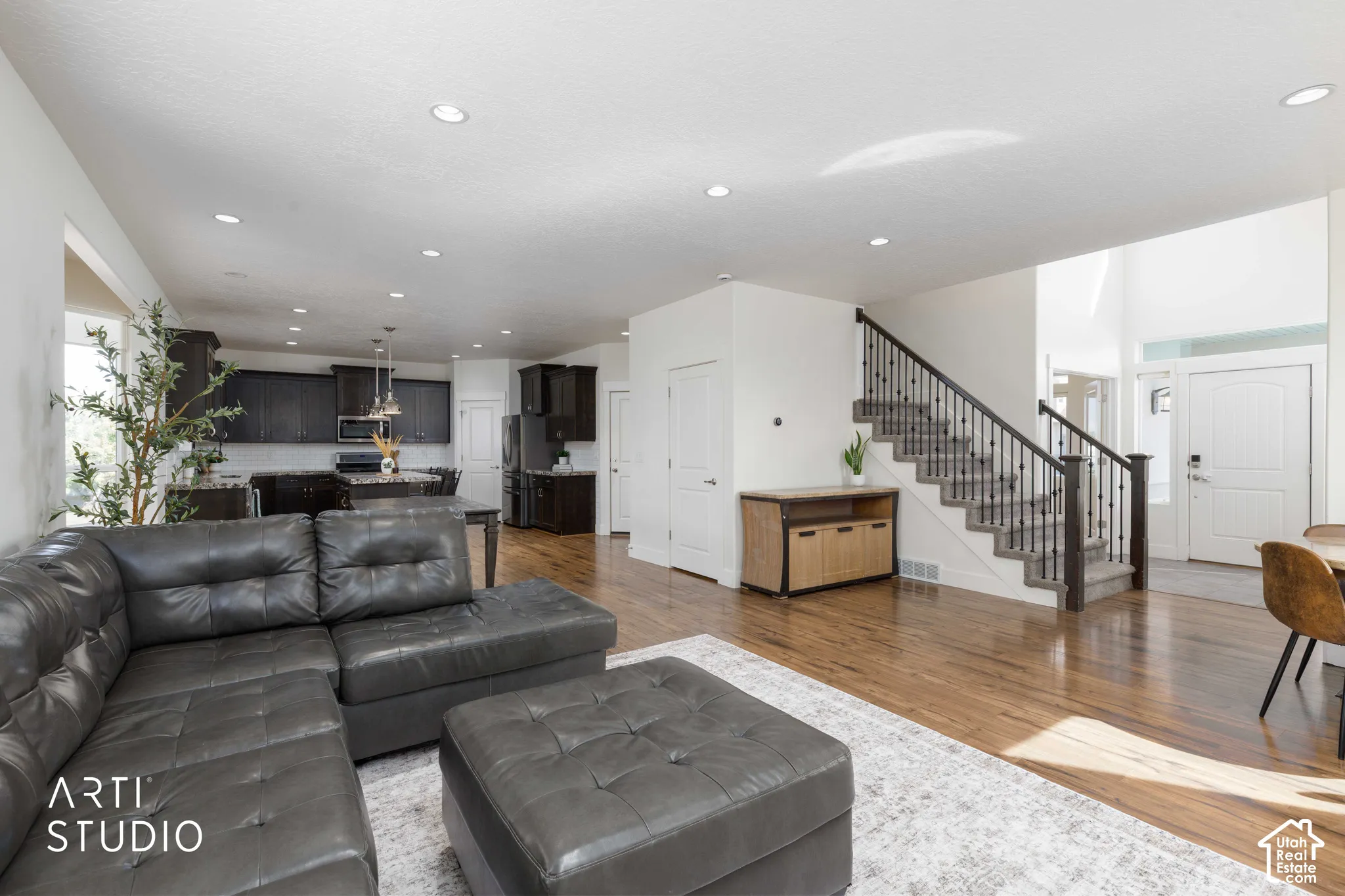 Expansive open-concept living area featuring wood-finish flooring, recessed lighting, a two-story entryway, and a staircase with wrought iron balusters