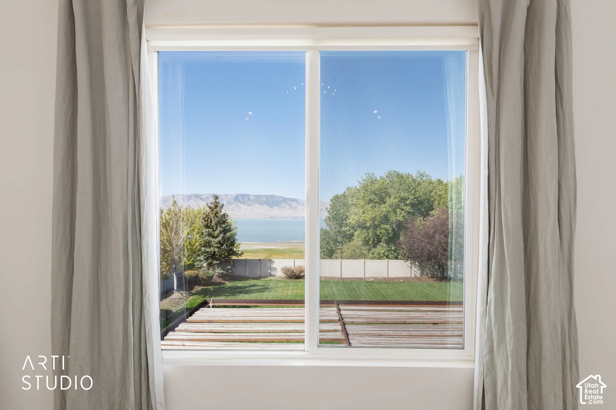 Large window with natural light, showcasing a landscaped backyard, distant lake, and mountainous backdrop