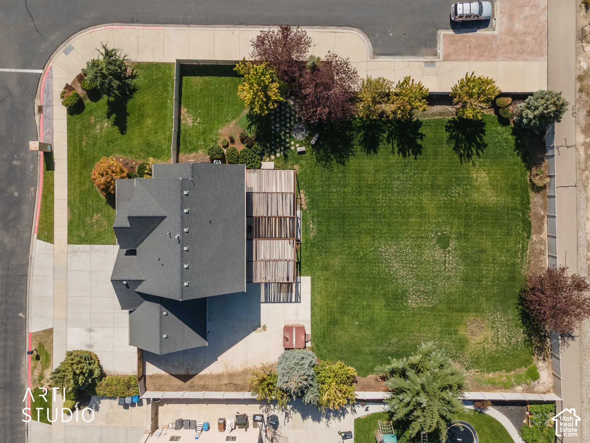 Shingle roof, extensive paved driveway, large grassy yard, mature trees, and a slatted pergola