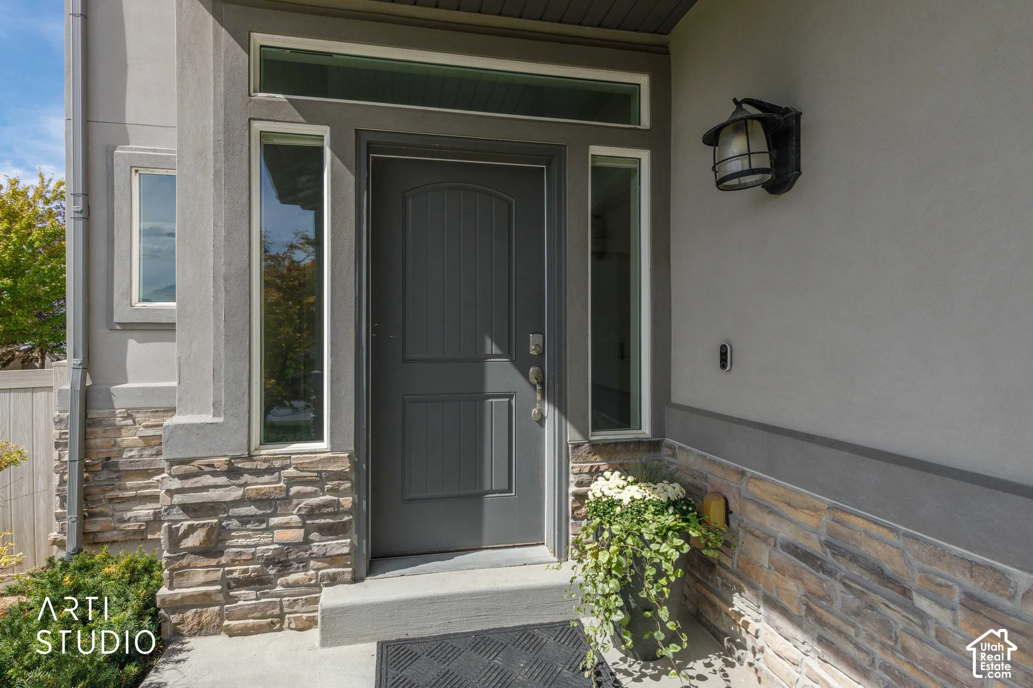 Front entry featuring a solid paneled door, stacked stone facade, and sconce lighting