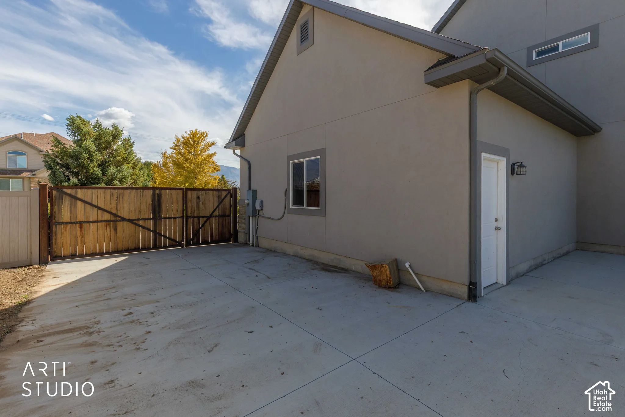 Spacious concrete driveway featuring a wood privacy gate, stucco exterior, and attached side entrance